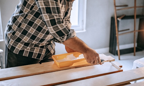 A white paint roller being used to paint wood.
